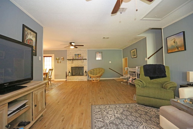 living area featuring ceiling fan, ornamental molding, a fireplace, and light wood-style flooring