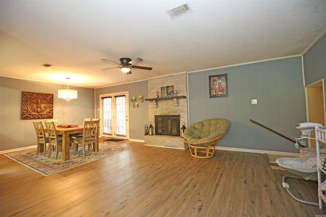 dining space featuring a brick fireplace, wood finished floors, visible vents, and crown molding