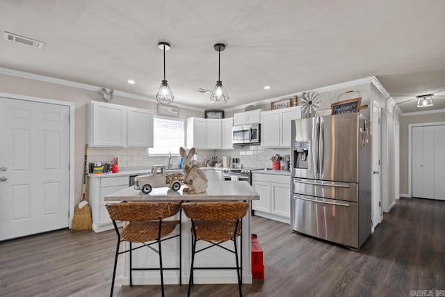 kitchen featuring white cabinets, a kitchen island, appliances with stainless steel finishes, decorative light fixtures, and light countertops