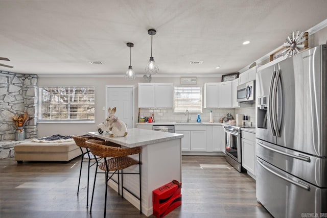 kitchen featuring decorative backsplash, appliances with stainless steel finishes, hanging light fixtures, white cabinetry, and a sink