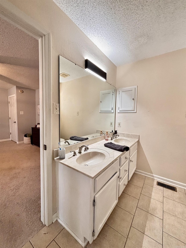 bathroom with double vanity, a textured ceiling, a sink, and tile patterned floors