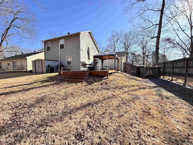 rear view of house featuring a fenced backyard, an outdoor structure, a gazebo, a wooden deck, and a shed