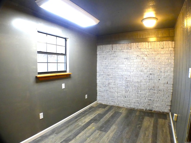 empty room with brick wall, baseboards, and wood finished floors