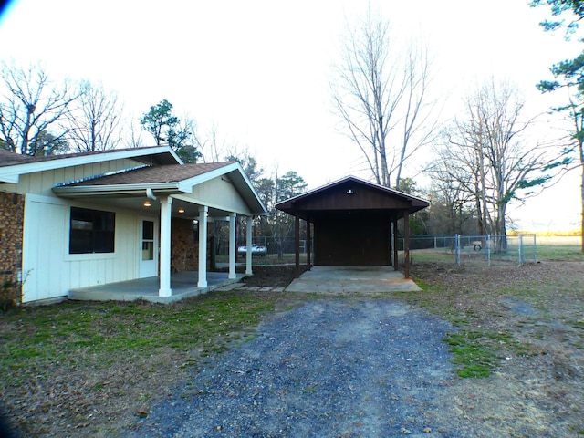 exterior space featuring driveway, roof with shingles, a patio area, and fence