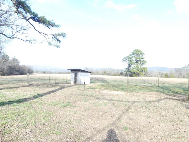 view of yard with a shed, a rural view, an outdoor structure, and fence