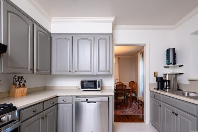 kitchen with gray cabinetry, stainless steel appliances, light countertops, light wood-type flooring, and crown molding