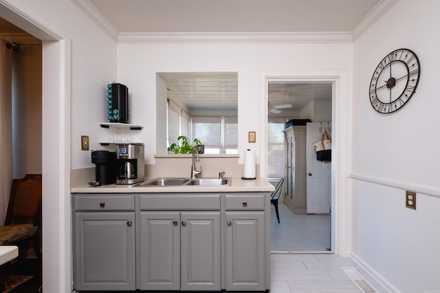 kitchen featuring visible vents, gray cabinets, crown molding, light countertops, and a sink