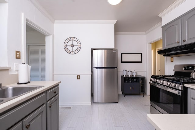 kitchen with under cabinet range hood, gray cabinetry, stainless steel appliances, light countertops, and ornamental molding