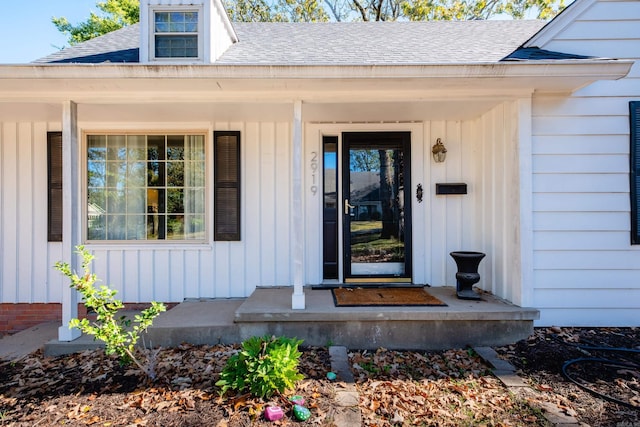 view of exterior entry featuring board and batten siding and roof with shingles