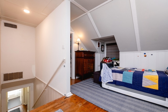 bedroom featuring wainscoting, visible vents, vaulted ceiling, and wood finished floors