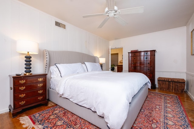 bedroom with dark wood-style floors, visible vents, a ceiling fan, and wainscoting