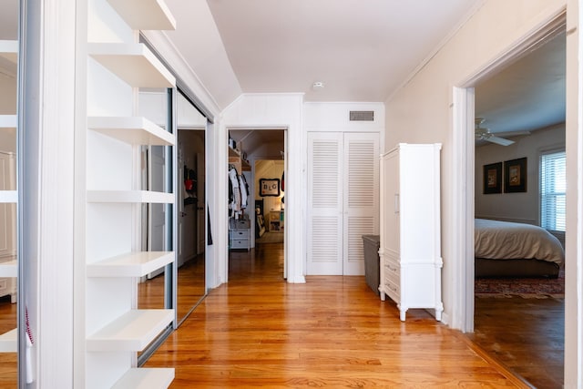 hall with light wood finished floors, visible vents, and ornamental molding