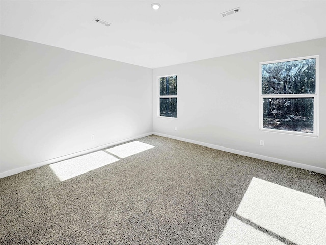 carpeted spare room featuring a healthy amount of sunlight, visible vents, and baseboards