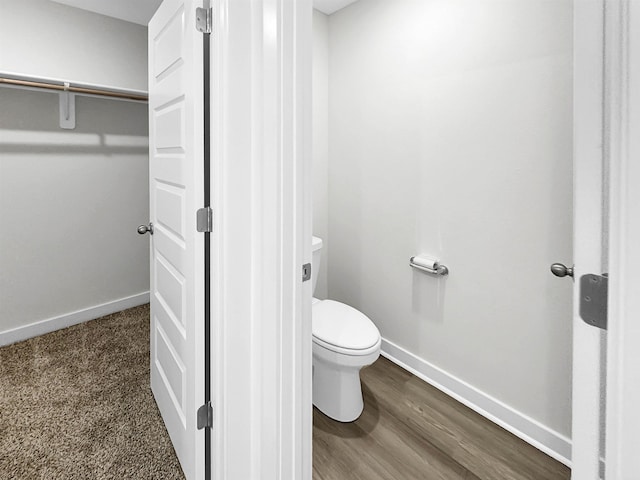 bathroom featuring a spacious closet, wood finished floors, toilet, and baseboards