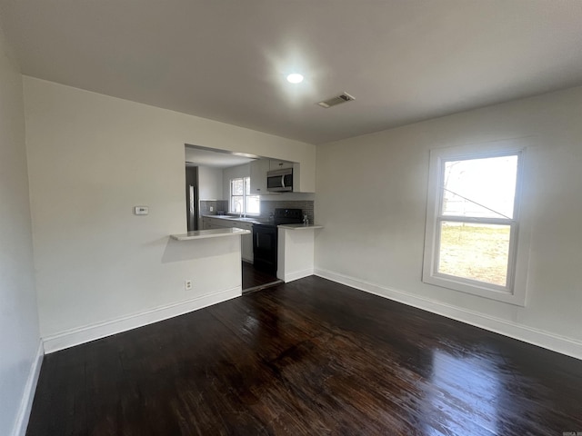 unfurnished living room with baseboards, visible vents, and dark wood-type flooring