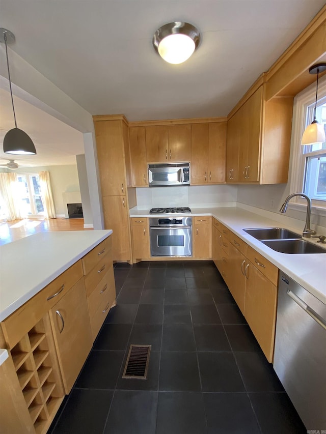 kitchen with light brown cabinets, stainless steel appliances, a sink, light countertops, and decorative light fixtures