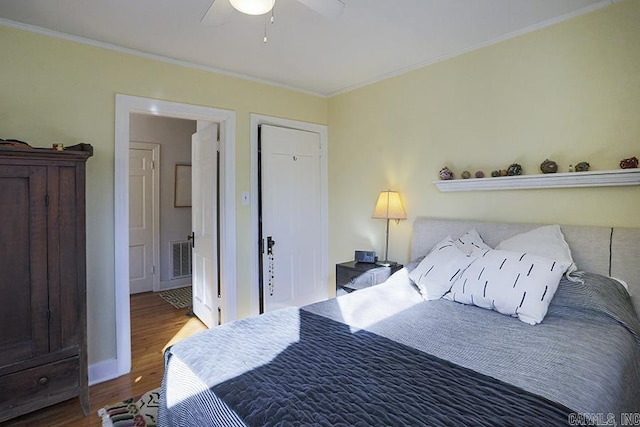 bedroom featuring ornamental molding, ceiling fan, ensuite bath, wood finished floors, and baseboards