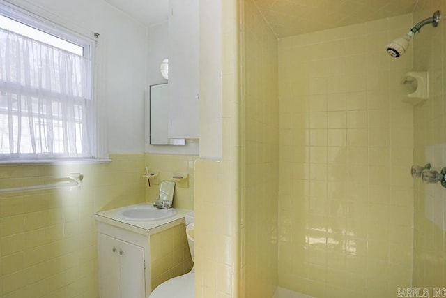 bathroom featuring toilet, vanity, tile walls, a shower, and wainscoting