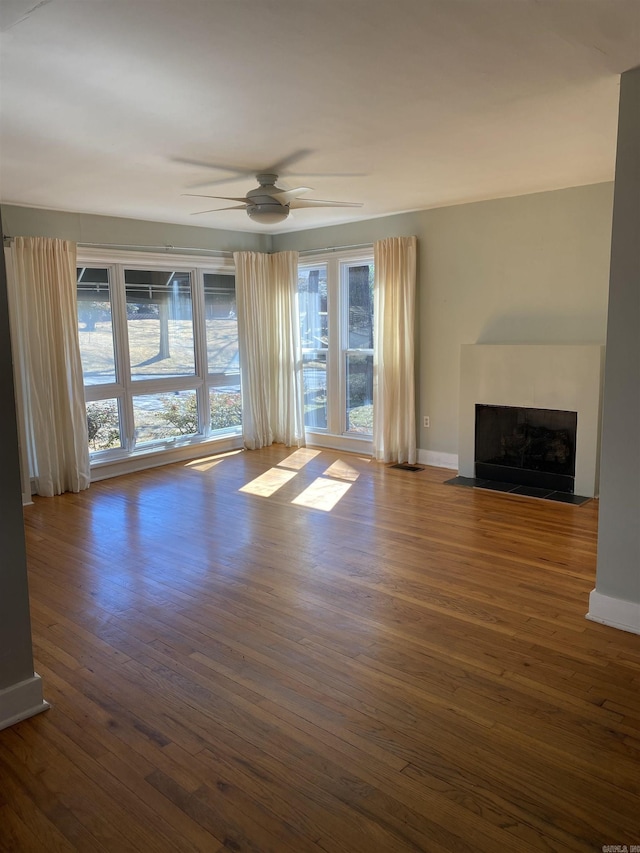 unfurnished living room featuring a fireplace with flush hearth, baseboards, ceiling fan, and dark wood-type flooring