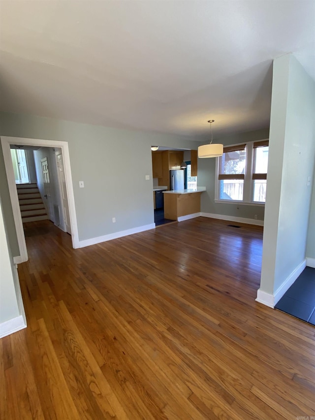 unfurnished living room featuring baseboards, visible vents, stairway, and dark wood-style flooring