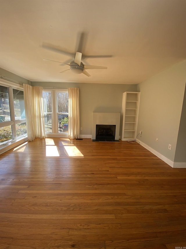 unfurnished living room featuring ceiling fan, dark wood-type flooring, a fireplace with flush hearth, and baseboards