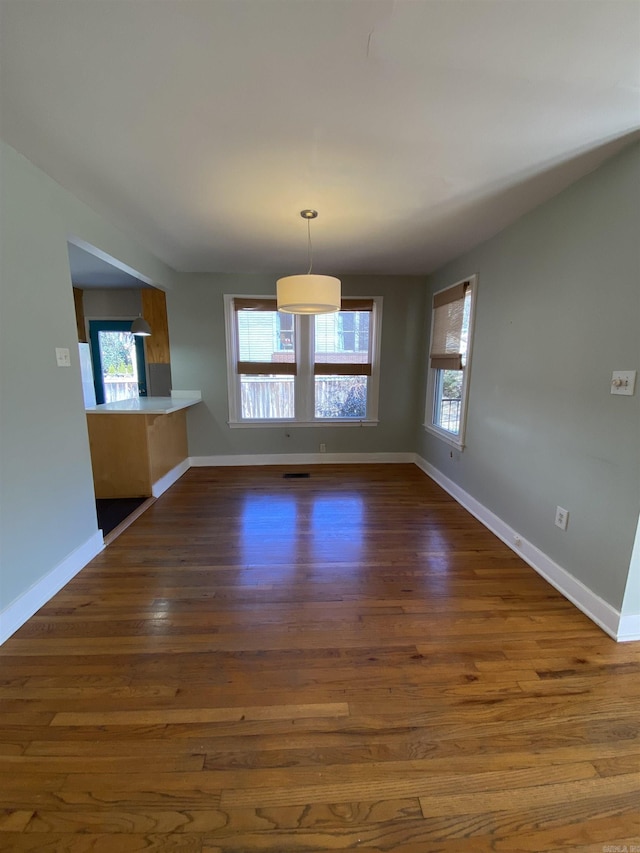 unfurnished dining area with dark wood-type flooring, visible vents, plenty of natural light, and baseboards