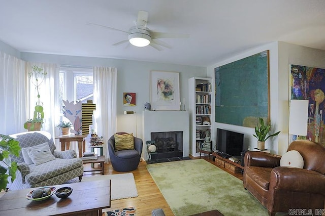 living area with a fireplace with flush hearth, ceiling fan, and wood finished floors