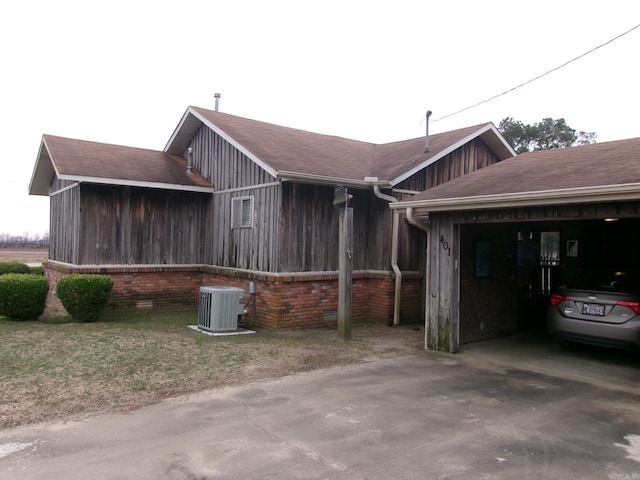 view of home's exterior featuring roof with shingles, brick siding, an attached garage, central AC unit, and driveway