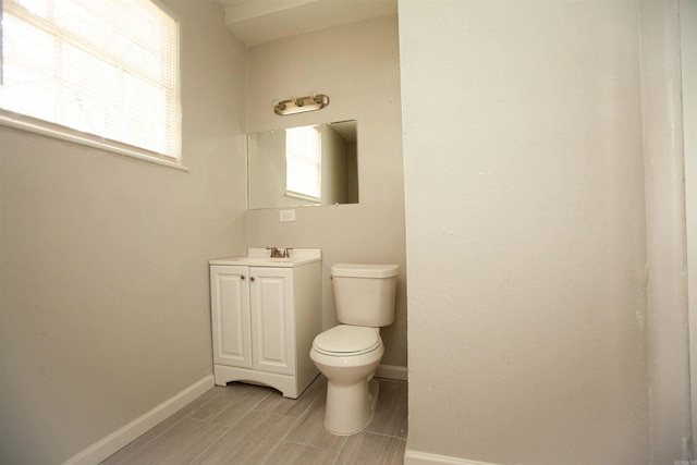 bathroom featuring baseboards, toilet, vanity, and a healthy amount of sunlight