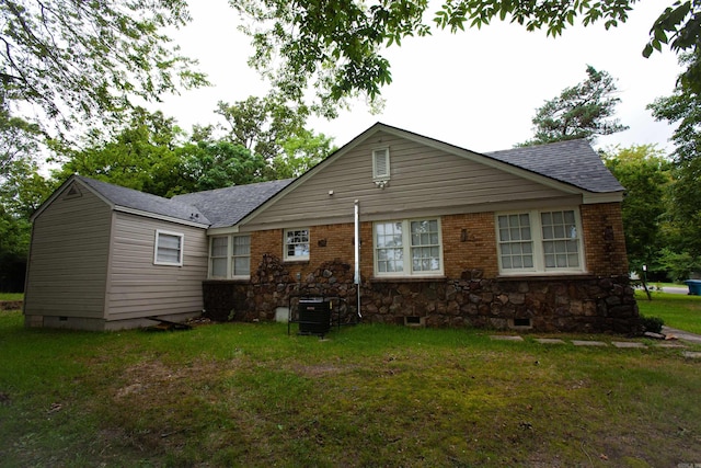 rear view of property with crawl space, a shingled roof, a lawn, and brick siding