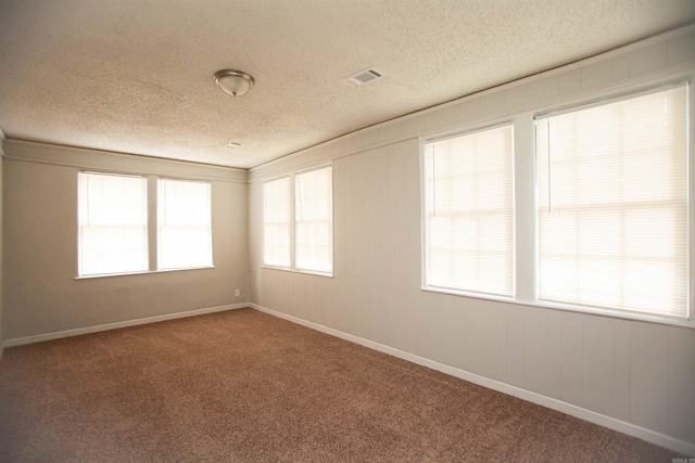 carpeted spare room featuring baseboards, visible vents, and a textured ceiling