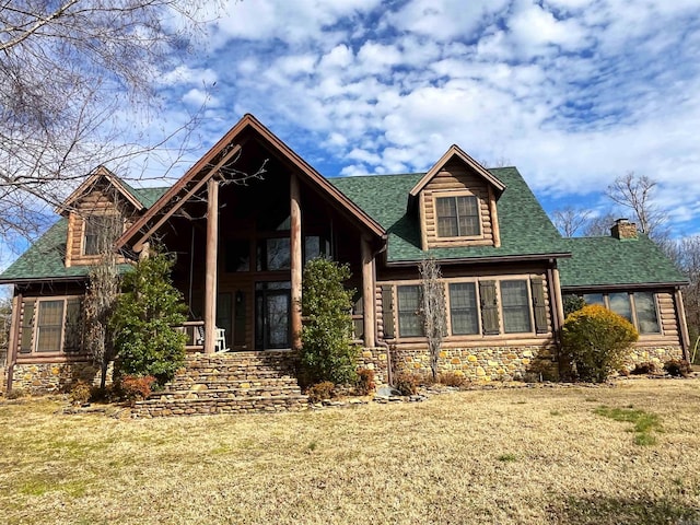 view of front of home with a shingled roof, stone siding, and a front lawn