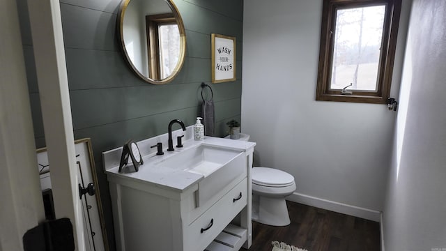 half bath featuring toilet, wood finished floors, vanity, and baseboards