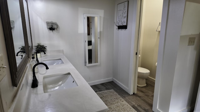 bathroom featuring double vanity, a sink, toilet, and wood finished floors