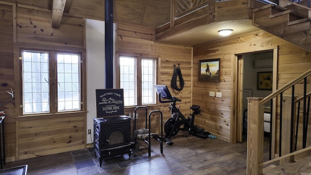 exercise area with dark wood finished floors, wooden ceiling, a wall mounted air conditioner, a wood stove, and wood walls