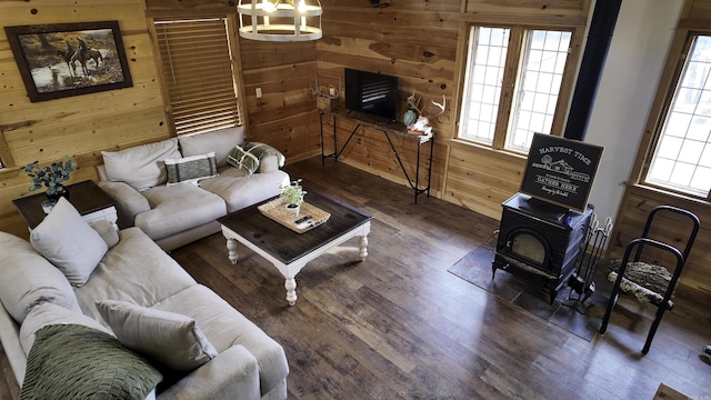 living room featuring wood walls, wood finished floors, a wood stove, and an inviting chandelier