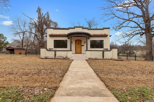 mediterranean / spanish-style home featuring a tiled roof, a front yard, fence, and stucco siding