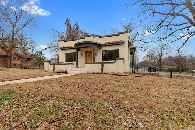 mediterranean / spanish house with a front lawn, a fenced front yard, a tile roof, and stucco siding