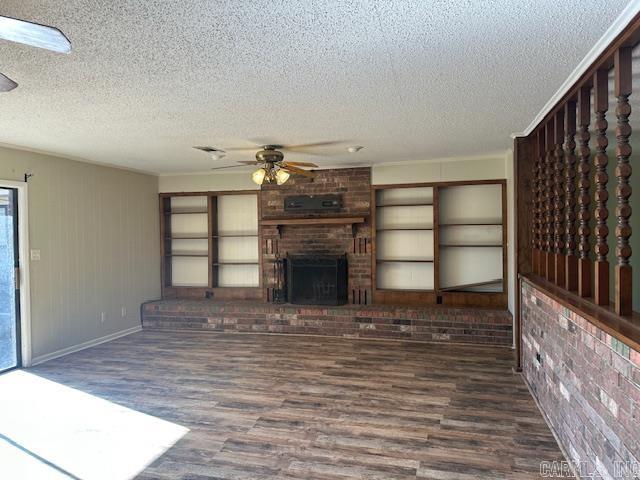 unfurnished living room with a fireplace, a ceiling fan, a textured ceiling, brick wall, and wood finished floors