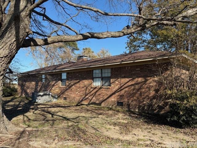 view of side of property with crawl space, a chimney, and brick siding