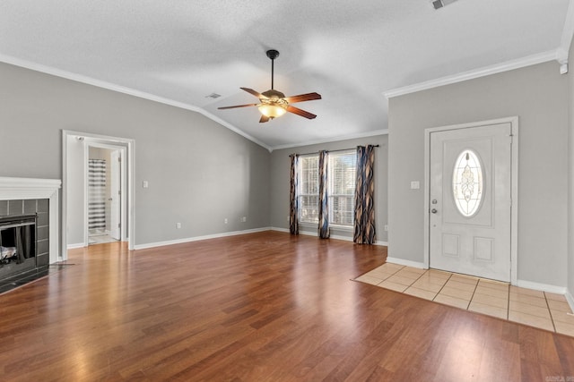 entryway featuring a ceiling fan, lofted ceiling, ornamental molding, light wood-style floors, and a fireplace