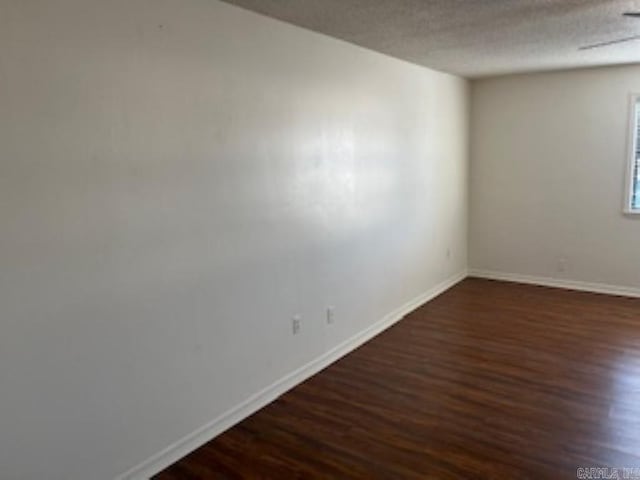 unfurnished room with baseboards, dark wood finished floors, and a textured ceiling