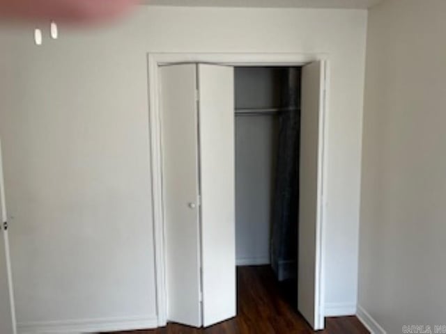 unfurnished bedroom with a closet, baseboards, and dark wood-style flooring