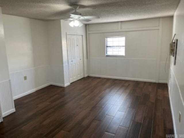 unfurnished room featuring a textured ceiling, dark wood-type flooring, a wainscoted wall, and a ceiling fan