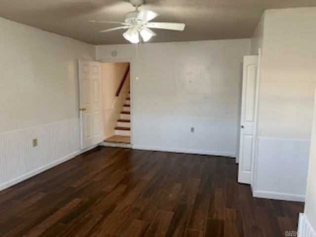 spare room with ceiling fan, stairway, dark wood-type flooring, and wainscoting