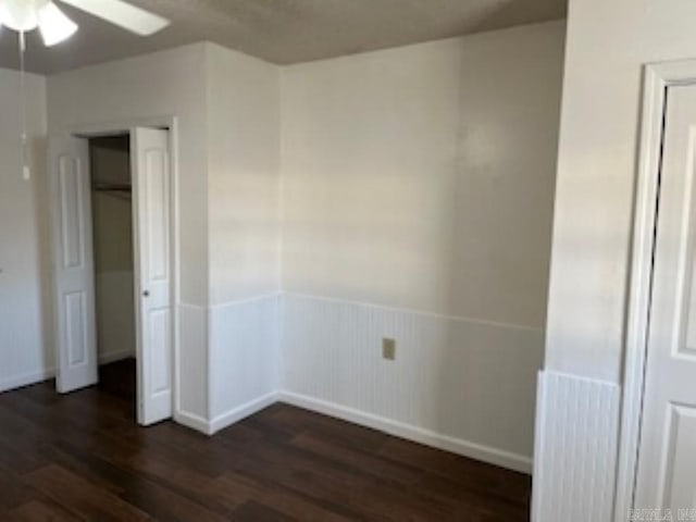 spare room with ceiling fan, dark wood-type flooring, and wainscoting