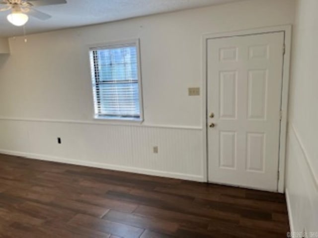 foyer with dark wood finished floors, a ceiling fan, and wainscoting