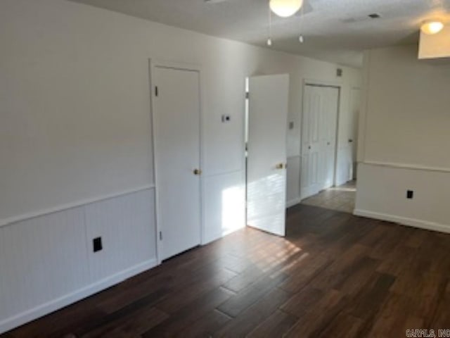 empty room featuring a wainscoted wall, ceiling fan, and dark wood finished floors