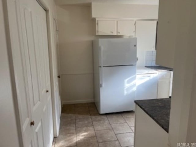 kitchen featuring light tile patterned flooring, white cabinetry, dark stone counters, and freestanding refrigerator