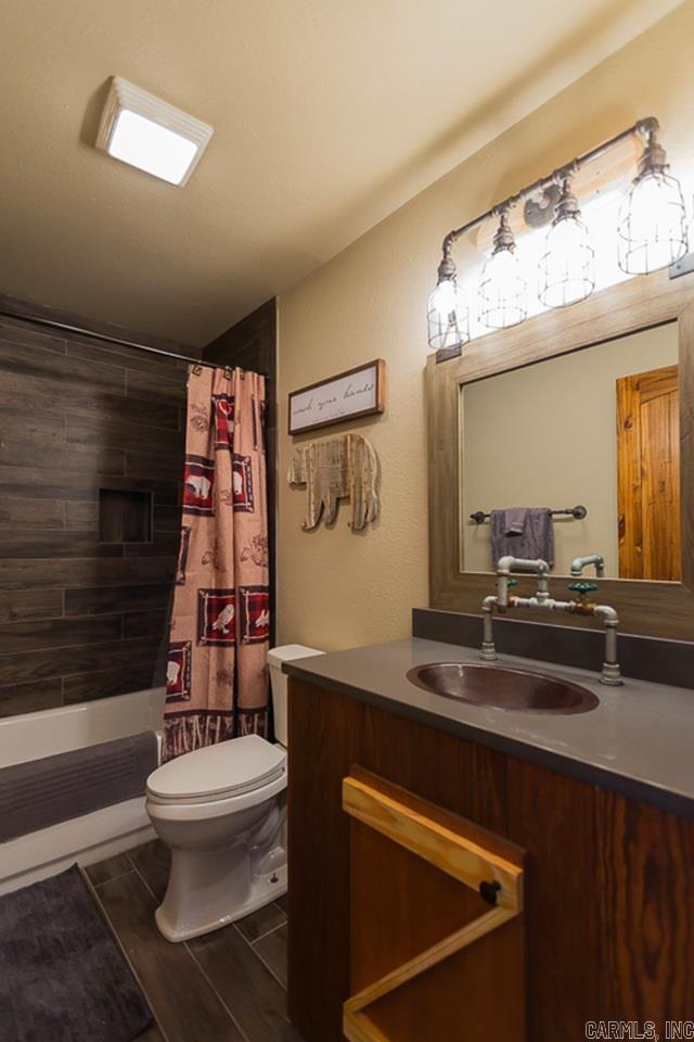 full bath featuring wood tiled floor, shower / bathtub combination with curtain, vanity, and toilet